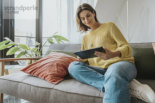Frau sitzt auf Sofa und benutzt Tablet-PC