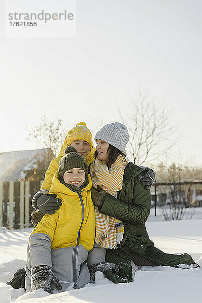Lächelnde Jungen mit Mutter  die im Winter auf Schnee sitzen