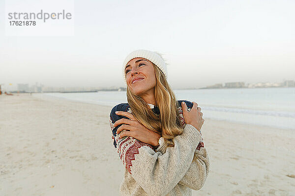 Lächelnde Frau in warmer Kleidung  die sich am Strand umarmt