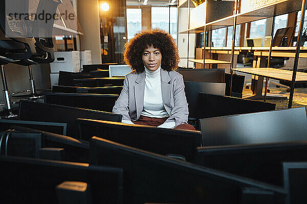 Geschäftsfrau sitzt inmitten von Computern am Arbeitsplatz