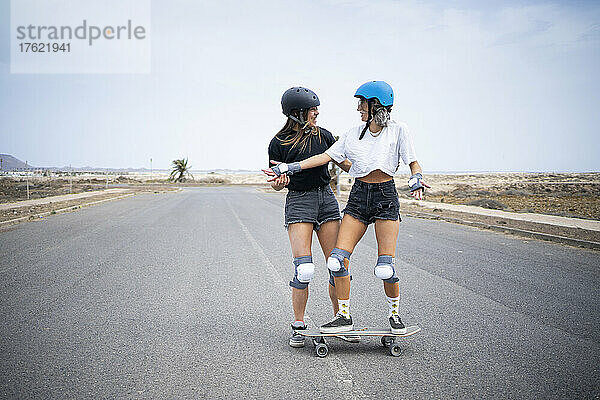 Junge Frau bringt einem Freund auf der Straße Skateboardfahren bei