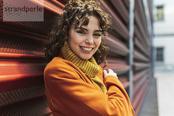 Lächelnde Frau im Rollkragenpullover an der Wand