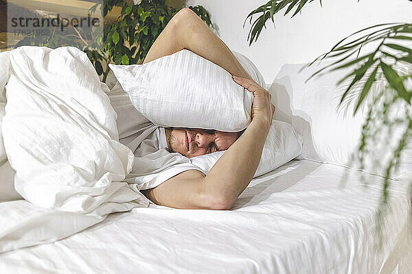 Man sleeping with pillow on head in bedroom at home