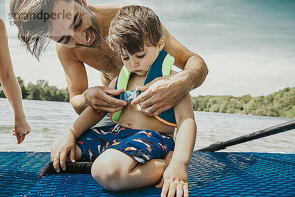 Vater befestigt Schwimmweste für Sohn im See