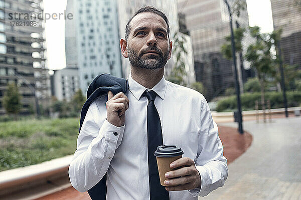 Porträt eines Geschäftsmannes  der mit Jacke und Einwegkaffeetasse in der Hand draußen steht