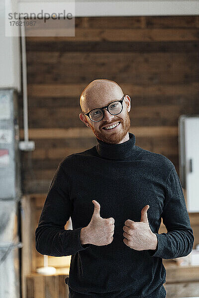 Happy young working man gesturing thumbs up in office