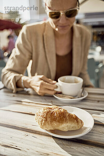 Frau trinkt an einem sonnigen Tag Kaffee im Straßencafé