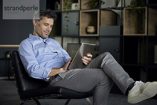 Geschäftsmann sitzt mit Tablet-PC auf Stuhl im Büro