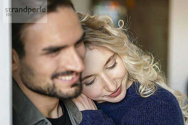 Lächelnde junge Frau mit blonden Haaren umarmt ihren Freund