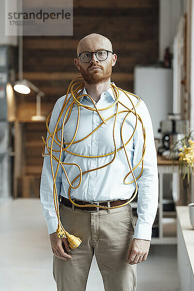 Junger Geschäftsmann mit Kabel bedeckt  der im Büro steht
