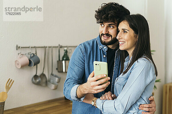Lächelndes Paar macht Selfie per Smartphone in der heimischen Küche
