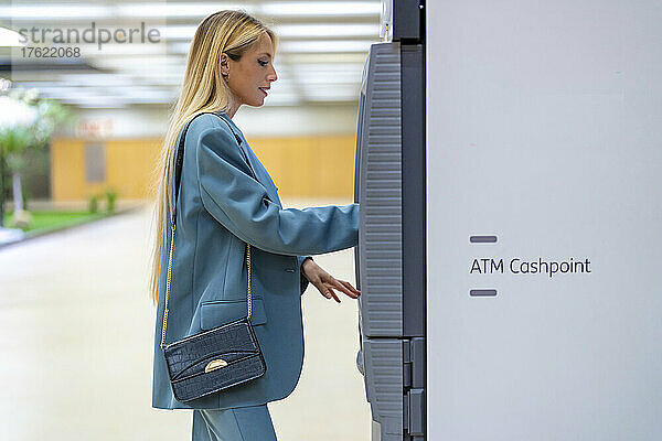 Blonde berufstätige Frau benutzt Geldautomaten an der U-Bahn-Station