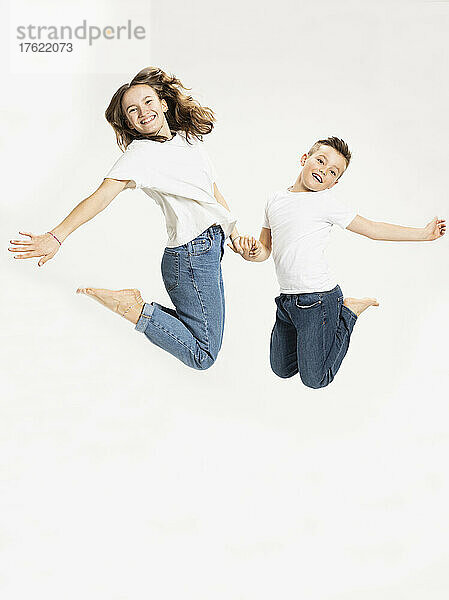 Cheerful brother and sister jumping against white background