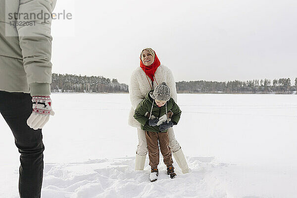 Lächelnde Frau umarmt Sohn und schaut Mann an  der auf Schnee steht