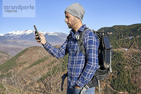 Mann steht mit der Hand in der Tasche und checkt an einem sonnigen Tag sein Smartphone