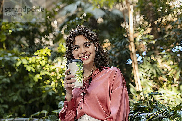 Lächelnde Frau mit Einwegkaffeetasse im Garten