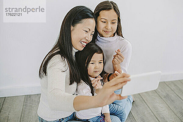Glückliche Mutter macht ein Selfie mit Töchtern  die zu Hause ein Herzzeichen zeigen