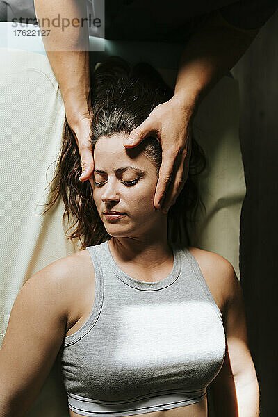 Physiotherapeut gibt einer Frau  die mit geschlossenen Augen liegt  eine Kopfmassage