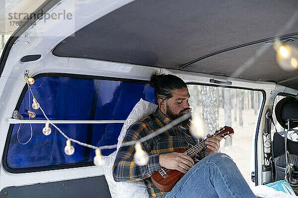 Bärtiger Mann  der Gitarre spielt  sitzt im Lieferwagen