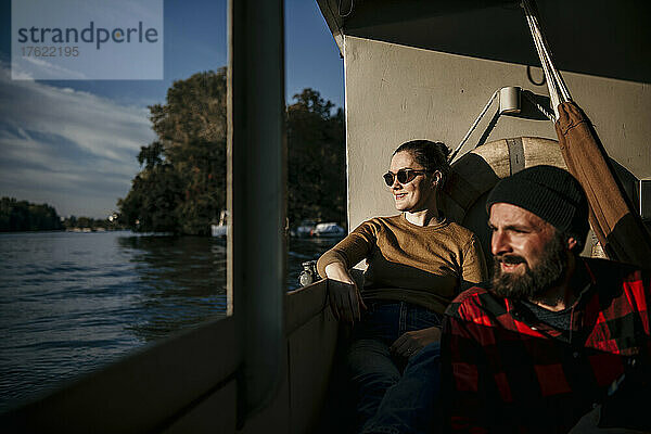 Smiling woman with man sitting on boat deck on sunny day