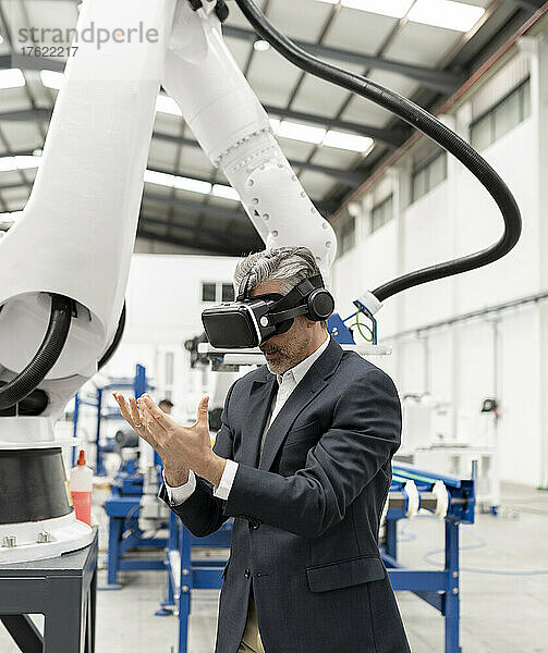 Geschäftsmann mit virtueller Realität steht mit gefalteten Händen in der Fabrik
