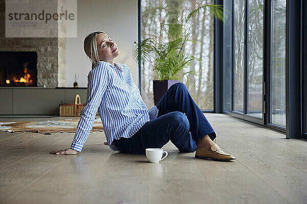 Blonde Frau mit geschlossenen Augen sitzt zu Hause auf dem Boden