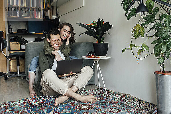 Glückliches junges Paar  das sich zu Hause im Wohnzimmer einen Laptop teilt