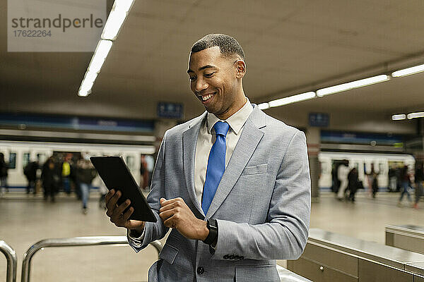 Glücklicher Geschäftsmann mit Tablet-PC am Bahnhof