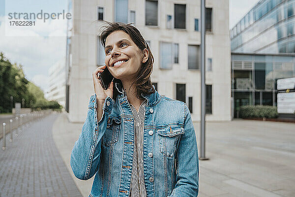 Glückliche Frau  die vor dem Gebäude mit dem Smartphone spricht