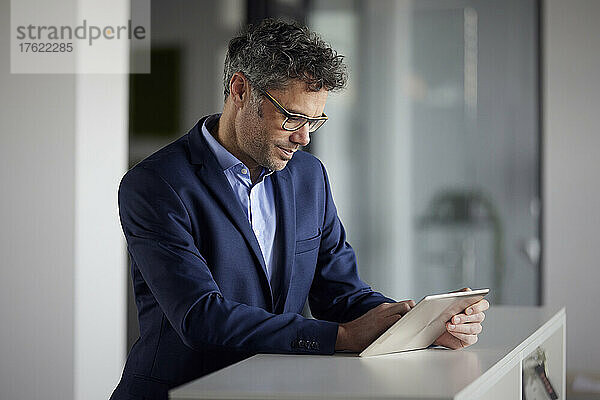 Geschäftsmann mit Brille und Tablet-PC steht am Schreibtisch im Büro