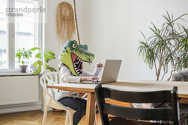 Mädchen mit Dinosauriermaske benutzt Laptop zu Hause