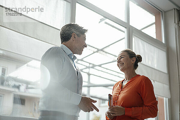 Happy businesswoman with businessman standing in front of window at office