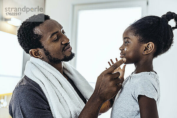 Vater trägt Tochter im Badezimmer Feuchtigkeitscreme auf