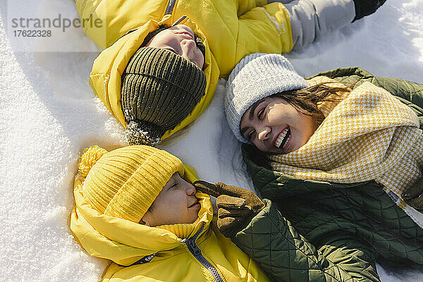 Happy mother touching boy nose lying on snow in winter