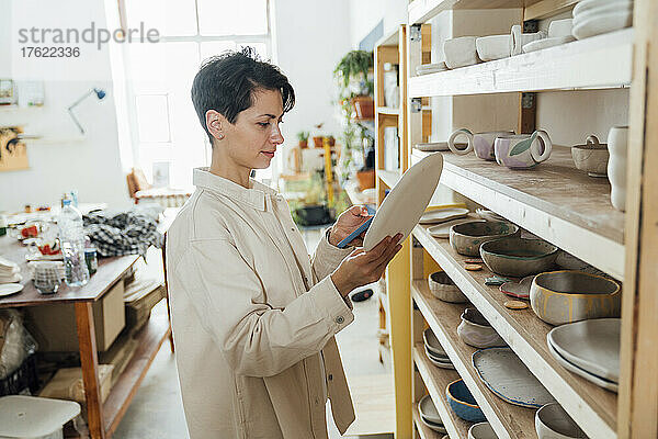Unternehmer mit Smartphone betrachtet Keramik in Werkstatt