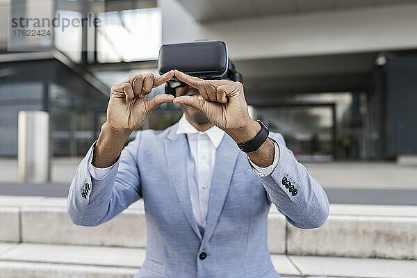 Geschäftsmann mit Virtual-Reality-Simulator gestikuliert auf Stufen vor Gebäude