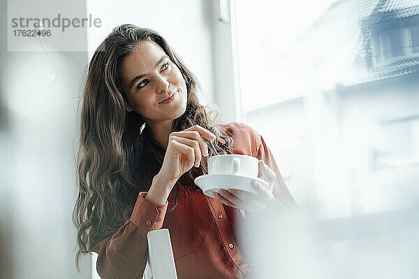 Lächelnde Frau mischt Kaffee und träumt im Café
