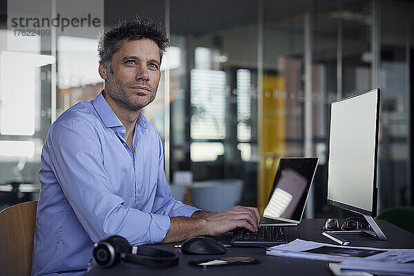 Nachdenklicher Geschäftsmann mit Desktop-PC sitzt im Büro