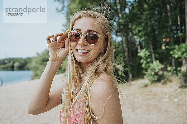 Lächelnde Frau mit Sonnenbrille am Seeufer