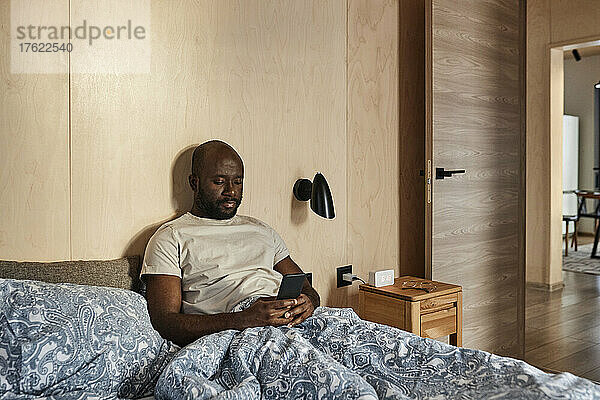 Junger Mann benutzt Smartphone im Schlafzimmer zu Hause