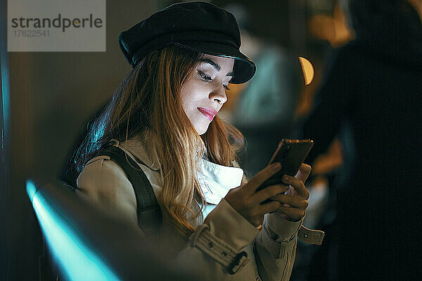 Smiling woman text messaging through smart phone at night