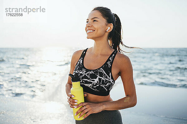 Happy young woman with water bottle on sunny day at beach
