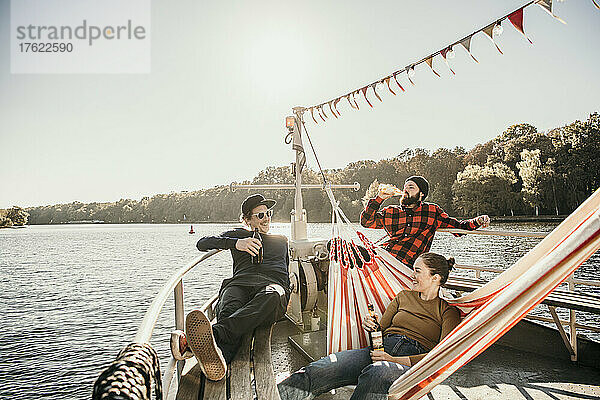 Happy friends enjoying beer sitting on boat bow
