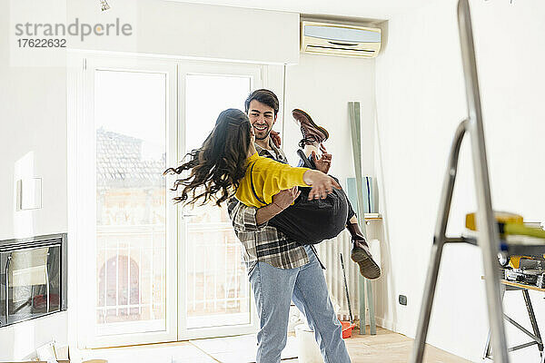 Man carrying girlfriend and dancing in living room at home