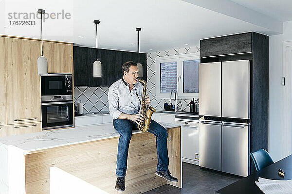 Musiker spielt Saxophon und sitzt zu Hause auf der Kücheninsel