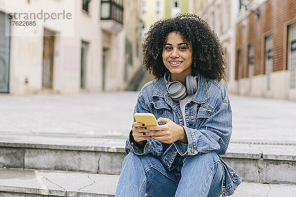 Lächelnde Frau mit Smartphone und Kopfhörer auf Stufen