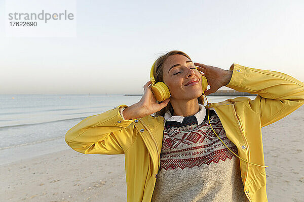 Glückliche Frau mit geschlossenen Augen  die Musik am Strand genießt