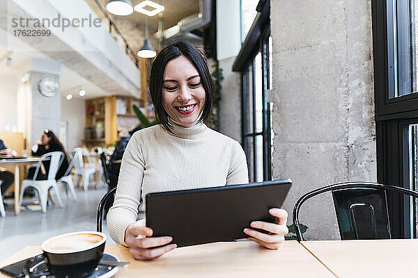 Glückliche Frau mit Tablet-PC sitzt im Café