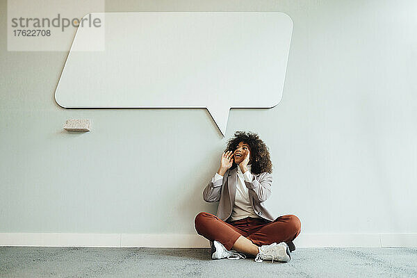 Geschäftsfrau schreit vor der Wand mit Sprechblasentafel im Büro