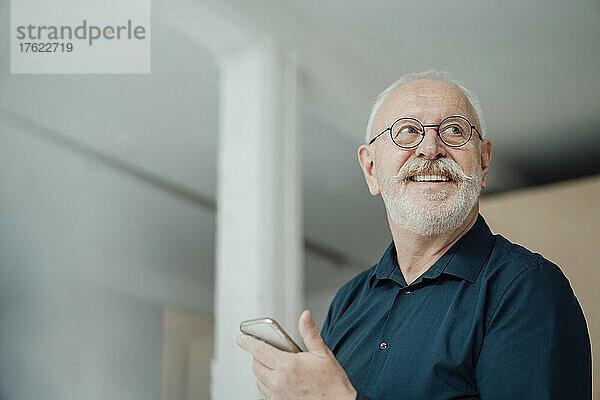 Glücklicher älterer Mann mit Smartphone im Büro